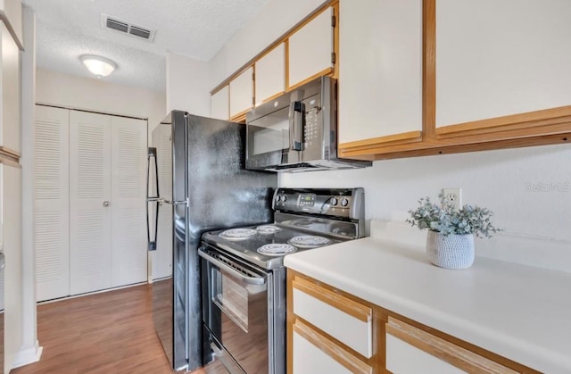 kitchen with visible vents, electric range, black microwave, light countertops, and light wood finished floors