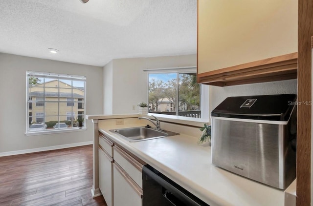 kitchen featuring a textured ceiling, wood finished floors, a sink, light countertops, and baseboards