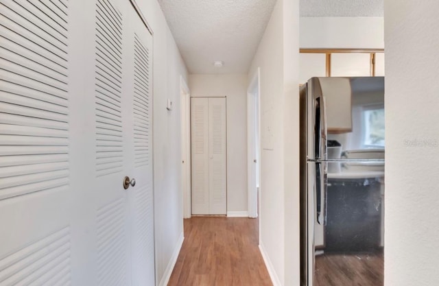hall featuring baseboards, a textured ceiling, and wood finished floors