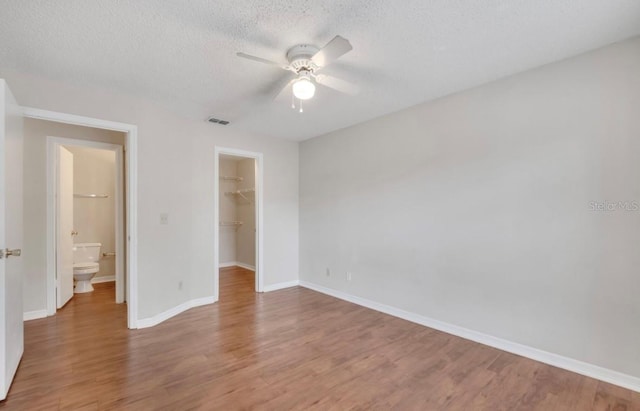 unfurnished bedroom featuring a closet, light wood-style floors, baseboards, a textured ceiling, and a spacious closet