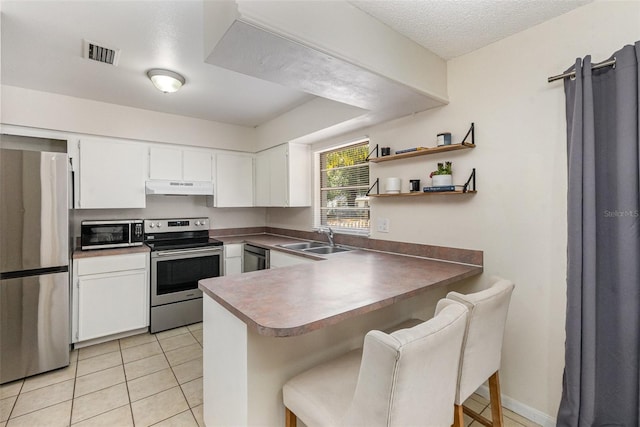 kitchen with appliances with stainless steel finishes, under cabinet range hood, a sink, a peninsula, and white cabinets