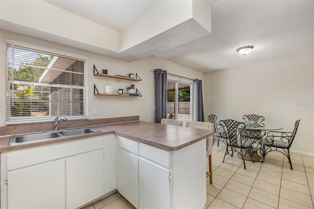 kitchen featuring a sink, light tile patterned floors, a peninsula, open shelves, and white cabinetry