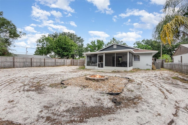 rear view of house with an outdoor fire pit, a sunroom, central AC unit, and a fenced backyard