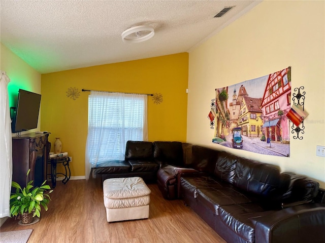 living area featuring wood finished floors, a textured ceiling, lofted ceiling, and visible vents