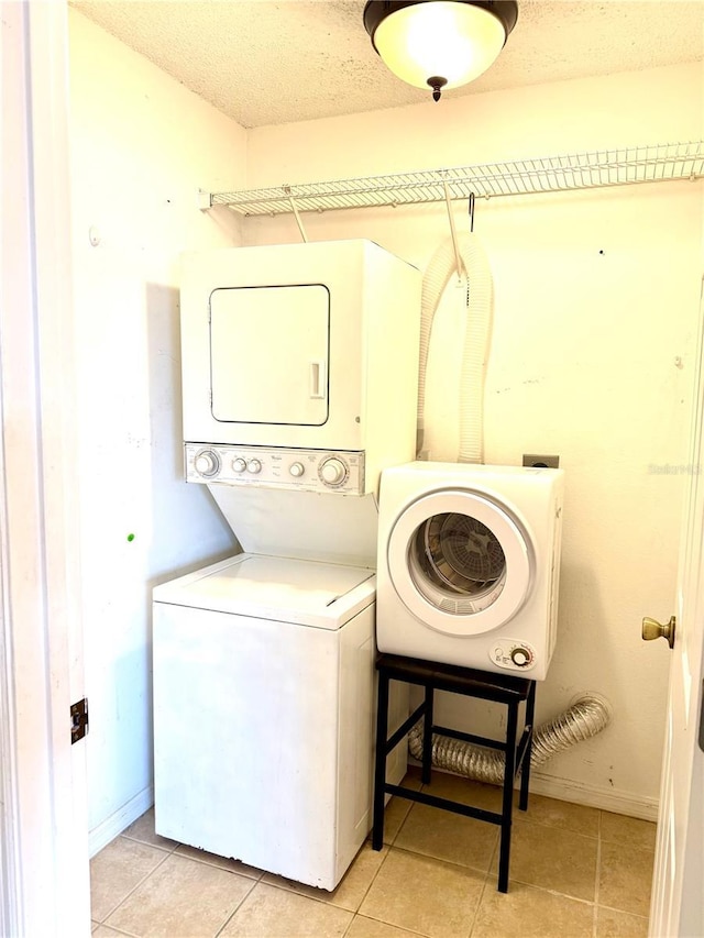 laundry room featuring laundry area, a textured ceiling, stacked washer / dryer, light tile patterned floors, and baseboards