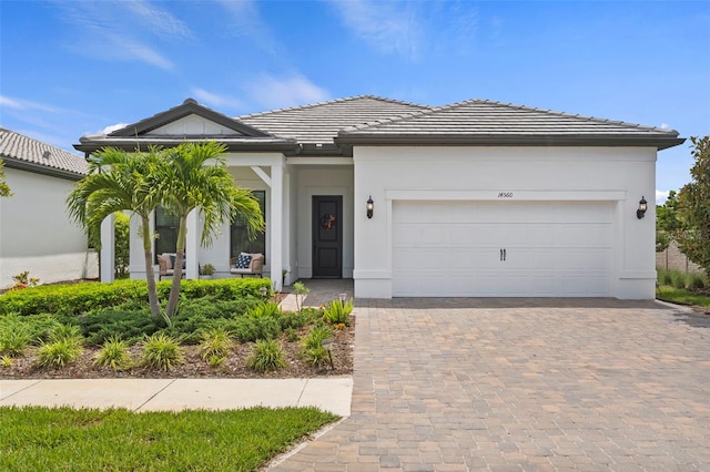 ranch-style home with a tiled roof, decorative driveway, stucco siding, and a garage
