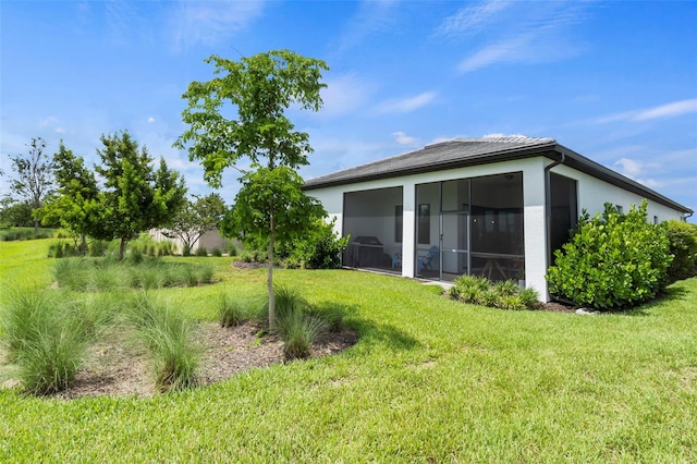 rear view of property with a yard, stucco siding, and a sunroom