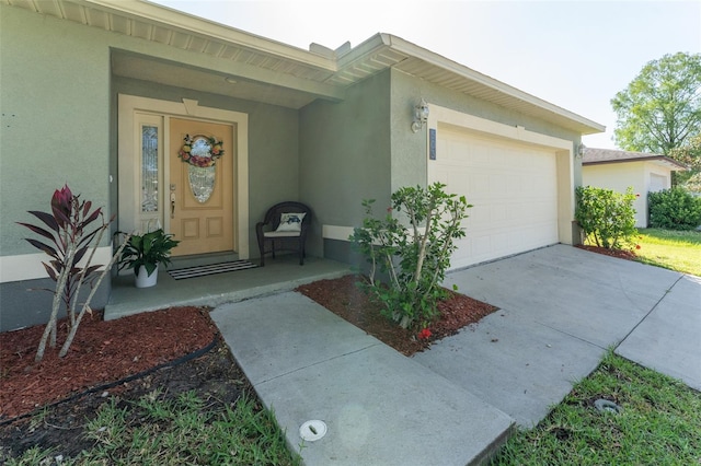 view of exterior entry with stucco siding, a garage, and driveway