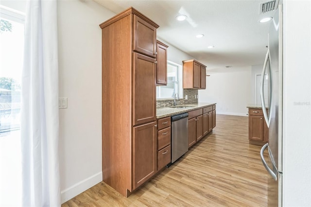 kitchen featuring appliances with stainless steel finishes, a sink, light wood-type flooring, baseboards, and light stone counters