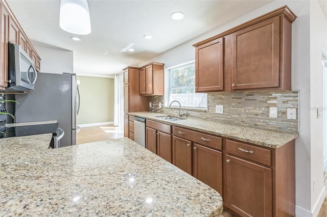 kitchen featuring stainless steel appliances, a sink, tasteful backsplash, light stone countertops, and baseboards