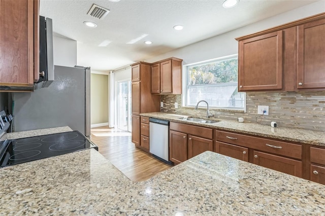 kitchen with appliances with stainless steel finishes, a sink, light wood-style floors, backsplash, and light stone countertops