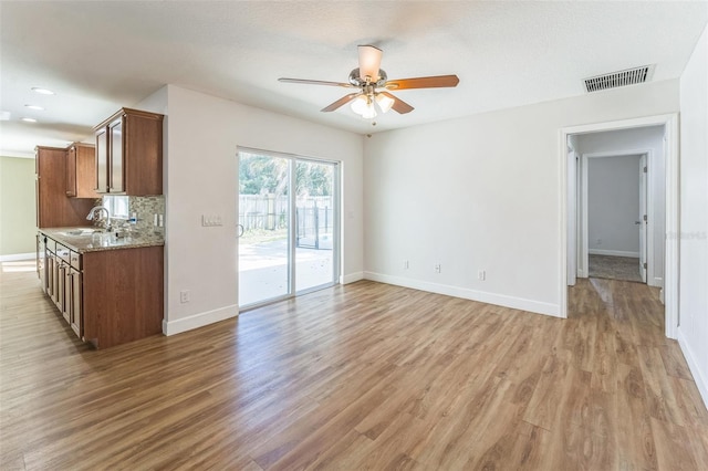 unfurnished living room featuring ceiling fan, a sink, light wood finished floors, and baseboards