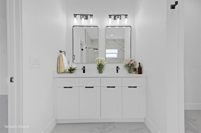full bath with marble look tile flooring, baseboards, a marble finish shower, and double vanity
