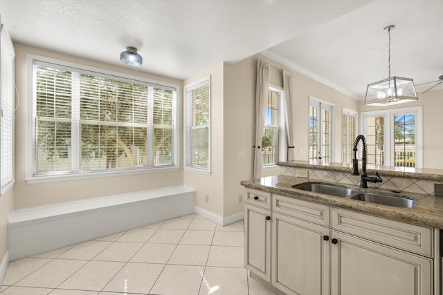kitchen with ornamental molding, light stone countertops, baseboards, a sink, and decorative light fixtures
