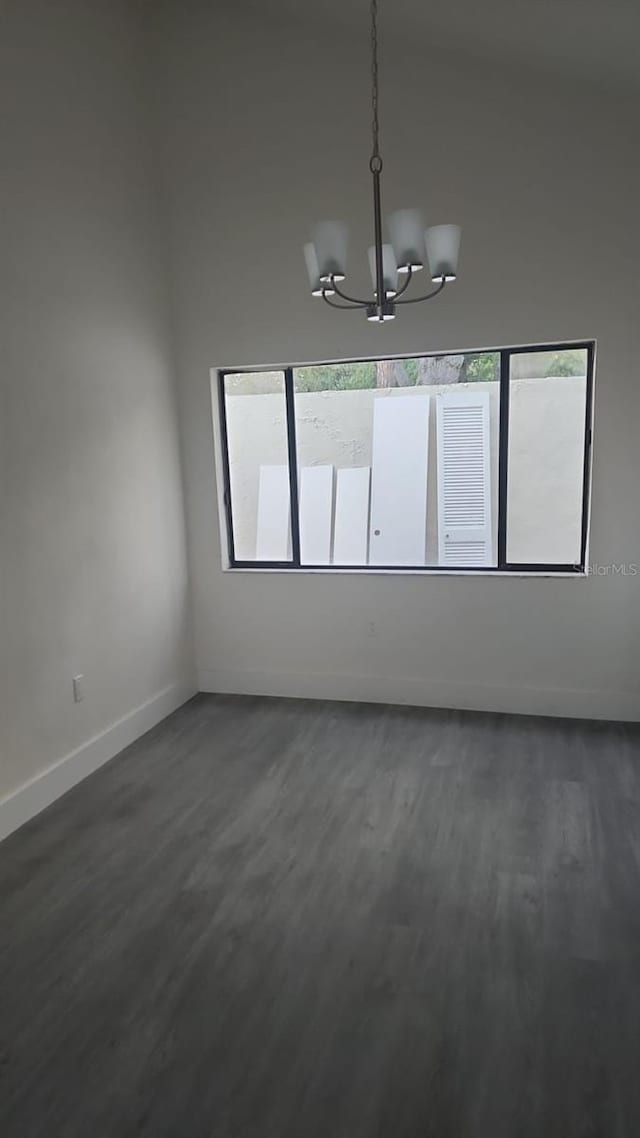 empty room featuring baseboards, a chandelier, and dark wood finished floors