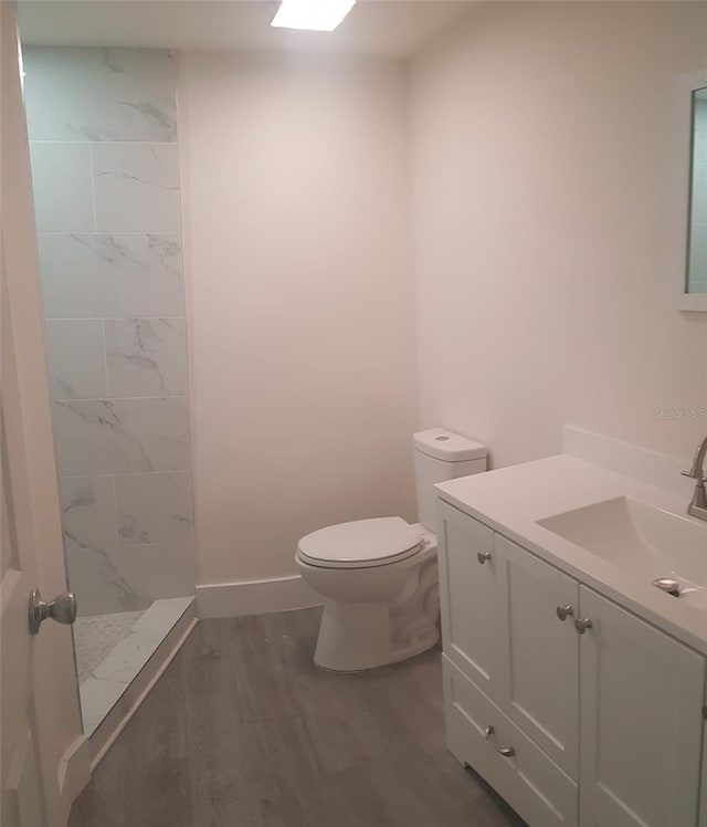 bathroom featuring vanity, a tile shower, toilet, and wood finished floors
