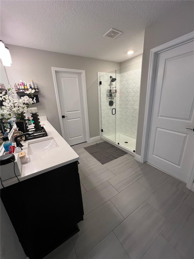 bathroom with visible vents, a sink, a textured ceiling, and a shower stall