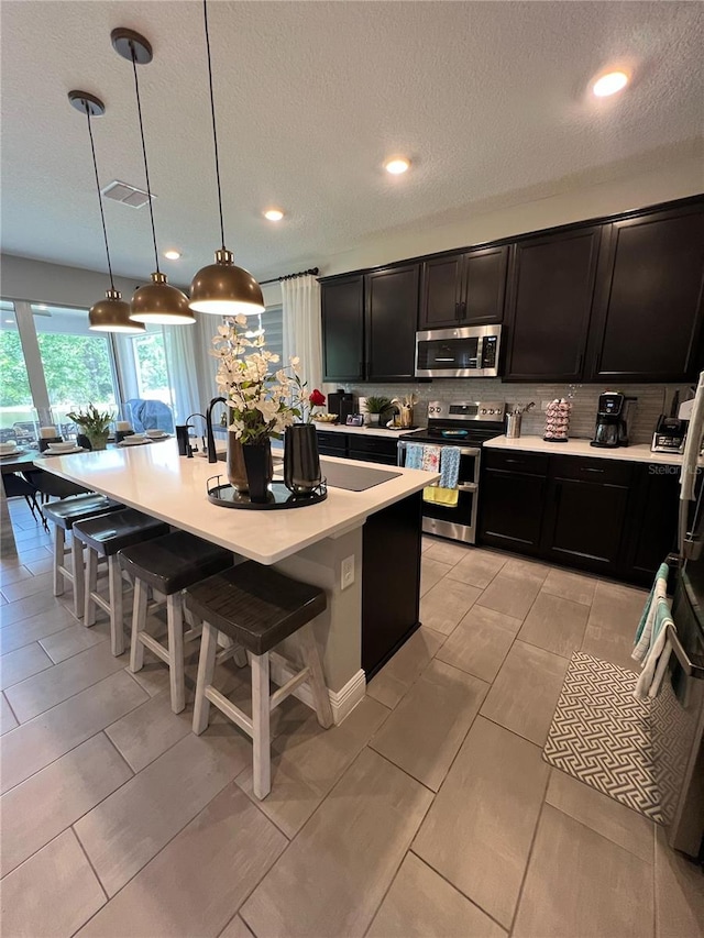 3920 Southern Vista Loop, Saint Cloud, FL 34772 - kitchen with appliances with stainless steel finishes, a breakfast bar area, light countertops, dark cabinets, and decorative backsplash