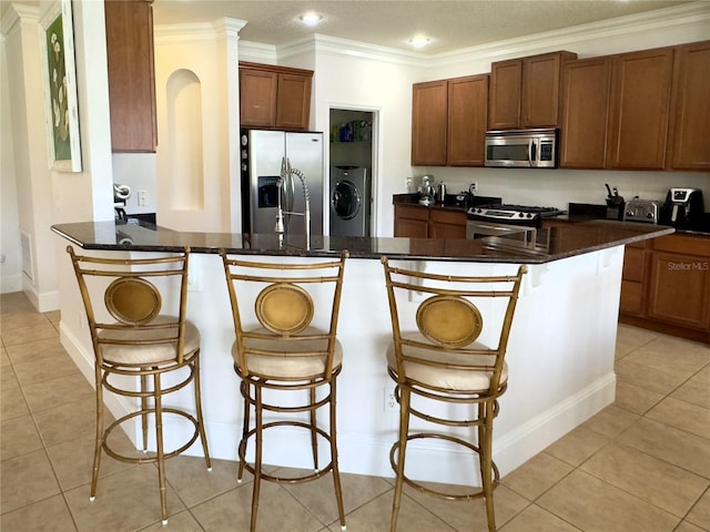 kitchen with washer / dryer, crown molding, appliances with stainless steel finishes, and a kitchen bar