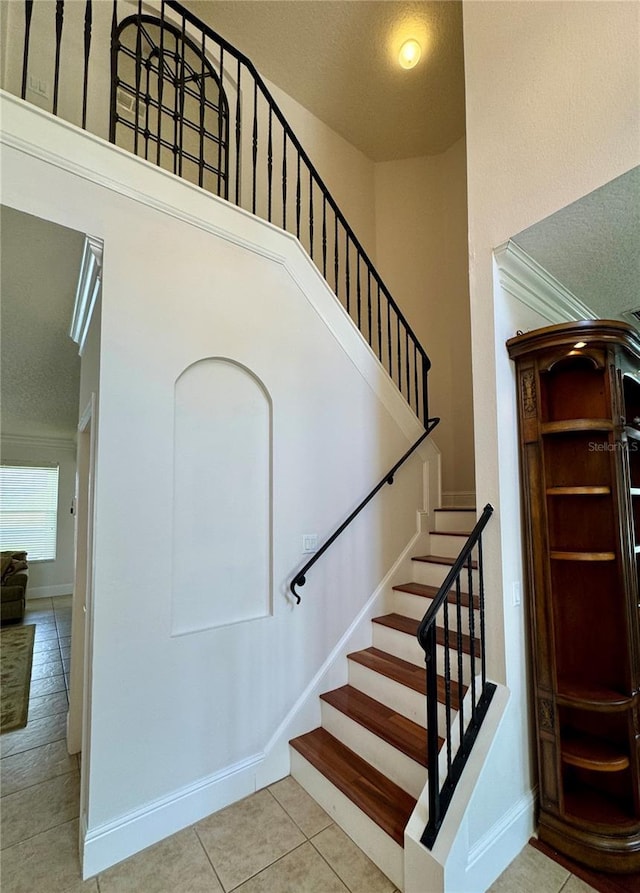 stairway with baseboards, a textured ceiling, tile patterned floors, and a towering ceiling