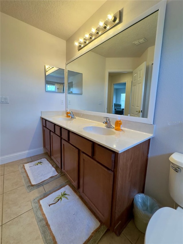 full bath with a sink, toilet, a textured ceiling, tile patterned flooring, and double vanity