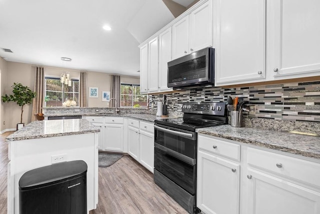 13044 Lakeshore Grove Dr, Winter Garden, FL 34787 - kitchen featuring stainless steel appliances, a sink, light wood finished floors, decorative backsplash, and white cabinetry