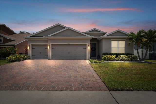 ranch-style house featuring an attached garage, decorative driveway, stucco siding, and a front lawn