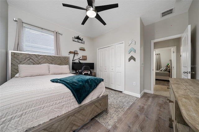 bedroom featuring a closet, a textured ceiling, baseboards, visible vents, and wood finished floors