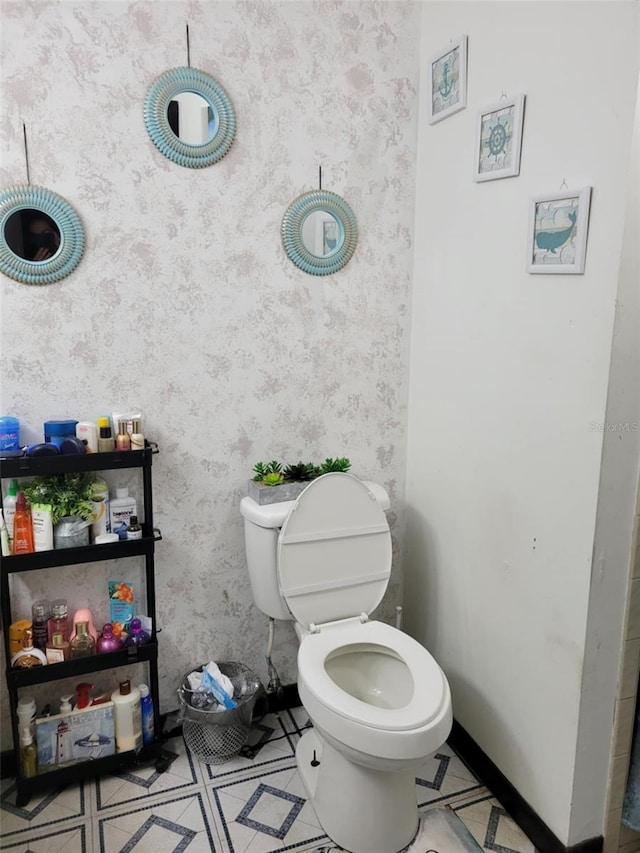bathroom featuring toilet, wallpapered walls, and baseboards