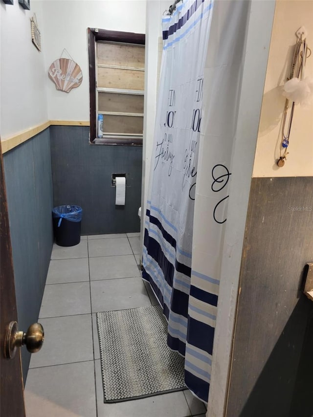 full bathroom with tile patterned floors, a shower with shower curtain, and a wainscoted wall