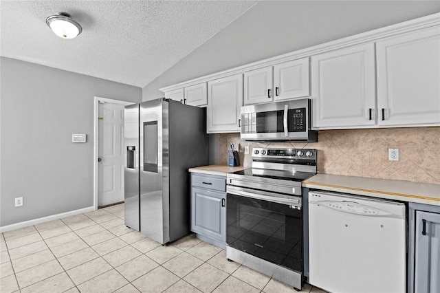 kitchen with appliances with stainless steel finishes, tasteful backsplash, vaulted ceiling, and a textured ceiling