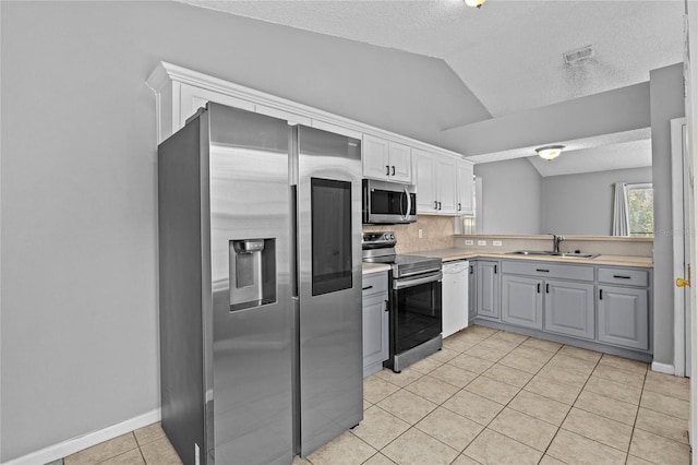 kitchen with gray cabinets, a textured ceiling, vaulted ceiling, light tile patterned floors, and stainless steel appliances