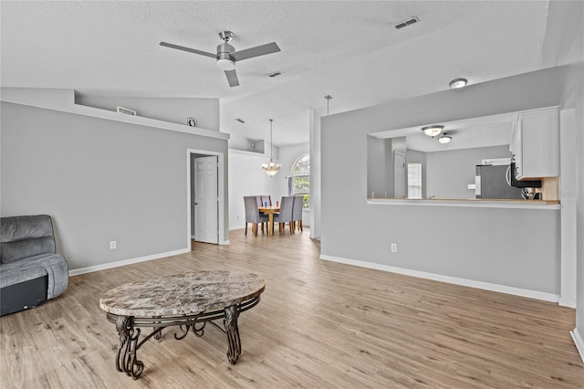 living room with light wood-style flooring, lofted ceiling, a textured ceiling, and visible vents