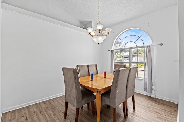 dining area with an inviting chandelier, baseboards, a textured ceiling, and wood finished floors