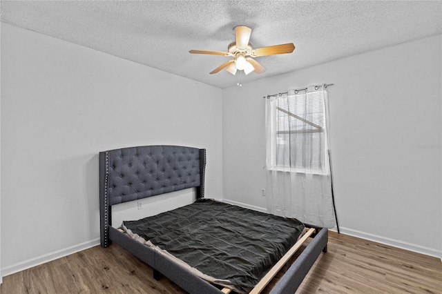 bedroom featuring baseboards, a ceiling fan, a textured ceiling, and wood finished floors