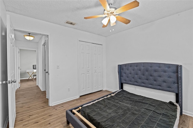 bedroom featuring a textured ceiling, baseboards, wood finished floors, visible vents, and a closet