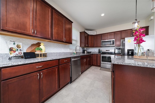 kitchen with a sink, pendant lighting, backsplash, appliances with stainless steel finishes, and light stone counters