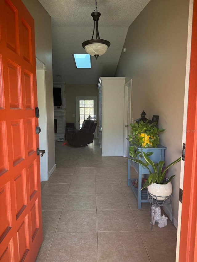 foyer entrance featuring a fireplace, light tile patterned flooring, a textured ceiling, and vaulted ceiling with skylight