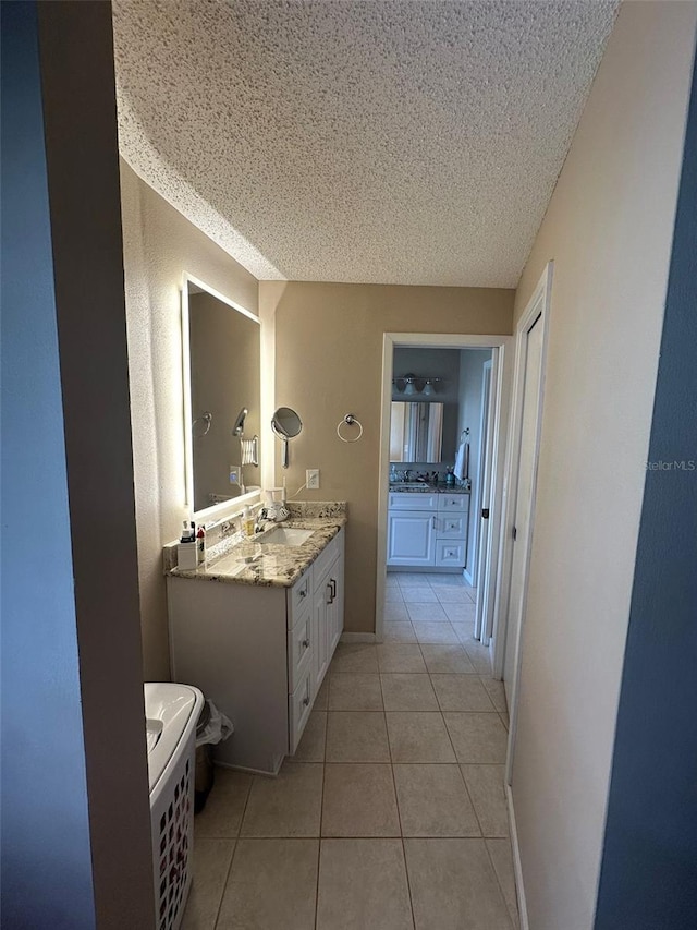 full bath featuring a textured ceiling, tile patterned flooring, two vanities, and a sink
