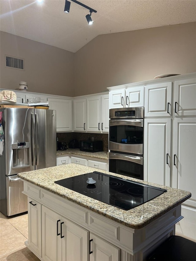 kitchen with a center island, visible vents, white cabinetry, vaulted ceiling, and stainless steel appliances