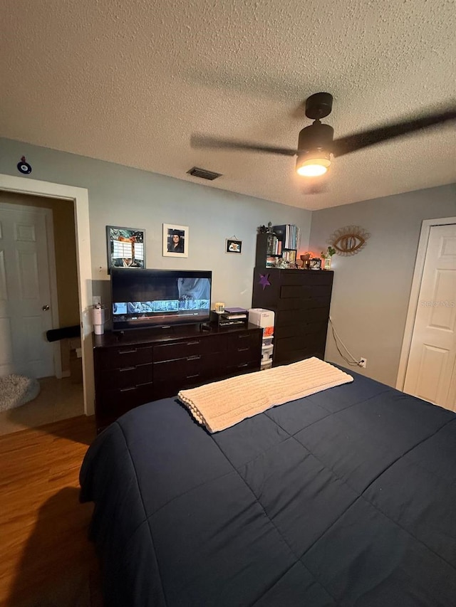 bedroom with ceiling fan, visible vents, a textured ceiling, and wood finished floors
