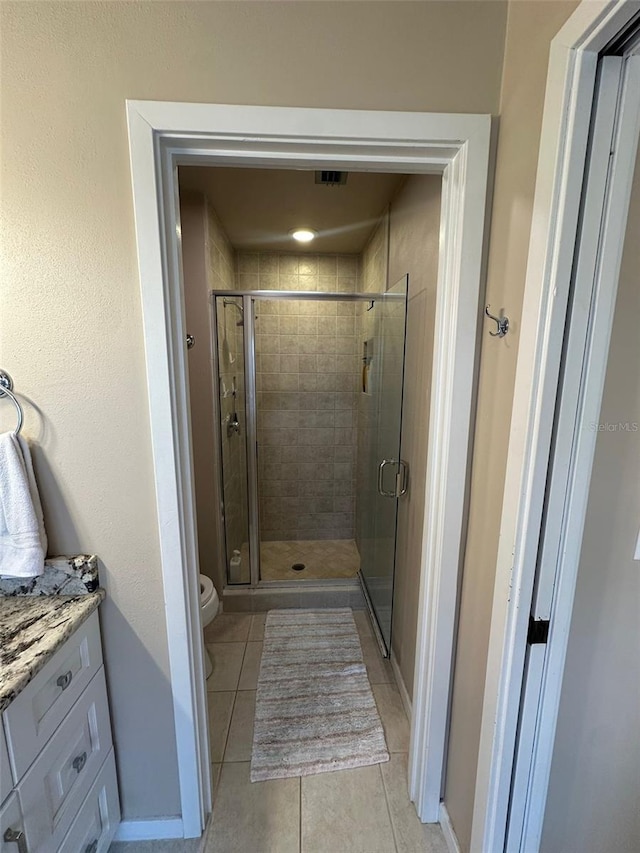 bathroom with toilet, vanity, tile patterned floors, a stall shower, and baseboards