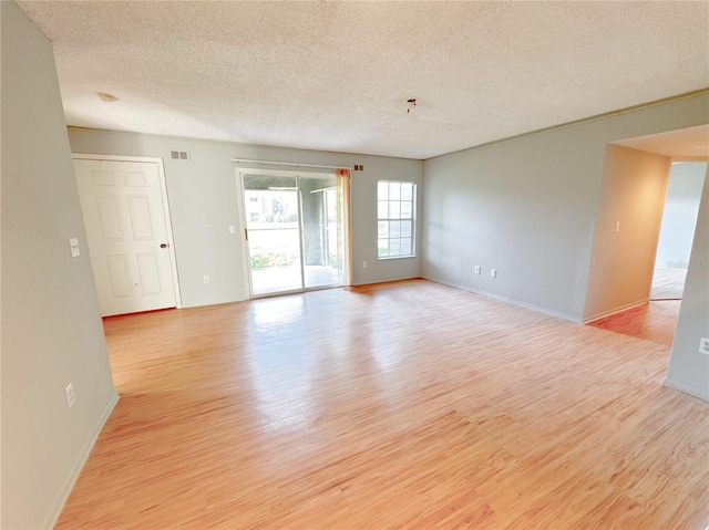 empty room featuring baseboards, light wood-style floors, visible vents, and a textured ceiling