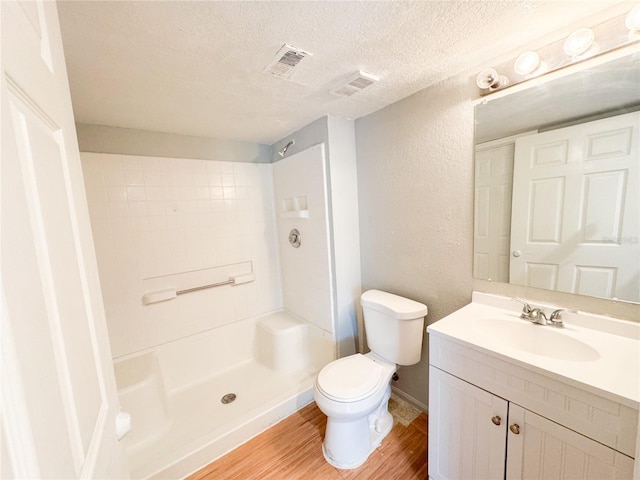 bathroom with toilet, vanity, wood finished floors, a shower, and a textured wall
