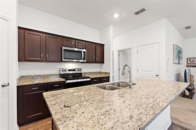 5816 Beefmaster Rd, Saint Cloud, FL 34771 - kitchen with stainless steel appliances, a sink, dark brown cabinets, a kitchen island with sink, and light stone counters
