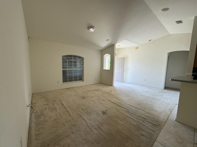 unfurnished room with light colored carpet, lofted ceiling, arched walkways, and visible vents