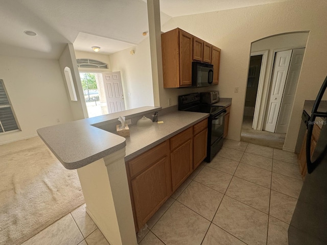 kitchen with light tile patterned floors, black appliances, brown cabinets, and a peninsula