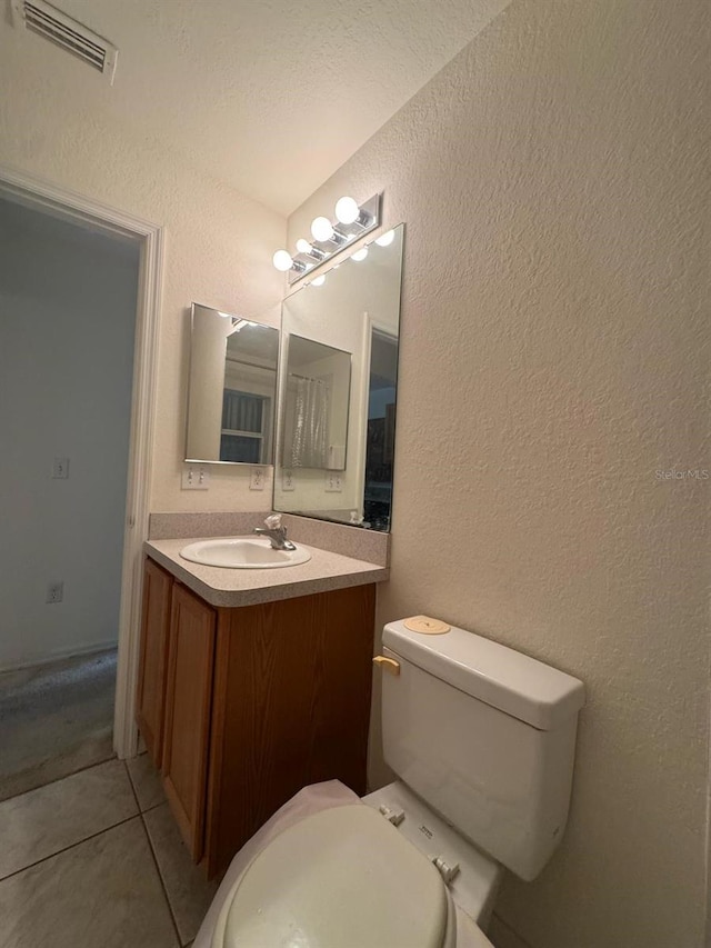 bathroom featuring toilet, visible vents, tile patterned flooring, vanity, and a textured wall