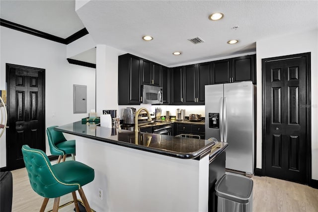 kitchen featuring stainless steel appliances, dark cabinets, visible vents, and a kitchen bar