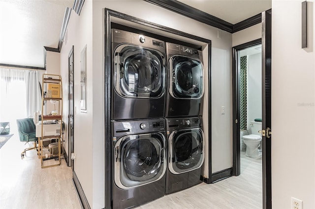 laundry room featuring baseboards, crown molding, stacked washer and clothes dryer, wood finished floors, and laundry area
